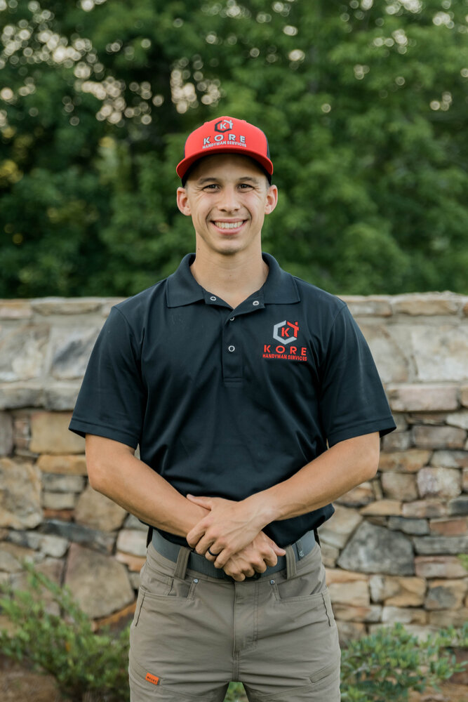 Kade Bloom with his black and red KORE workshirt and hat, standing next to his pickup truck, arm over the back, with his black and red KORE workshop trailer in the back.