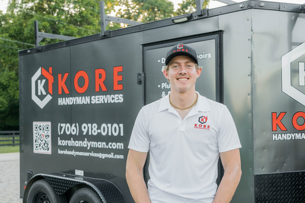Kade Bloom's smiling employee Nathaniel standing in a white shirt with the red and black KORE logo, with the black and red KORE workshop trailer behind him