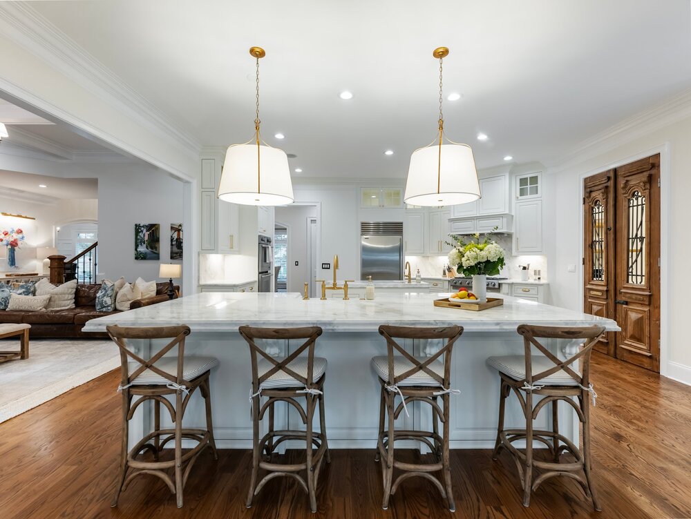 Spacious kitchen with white marble-top breakfast island and hanging ceiling lamps with wood bar seats in front