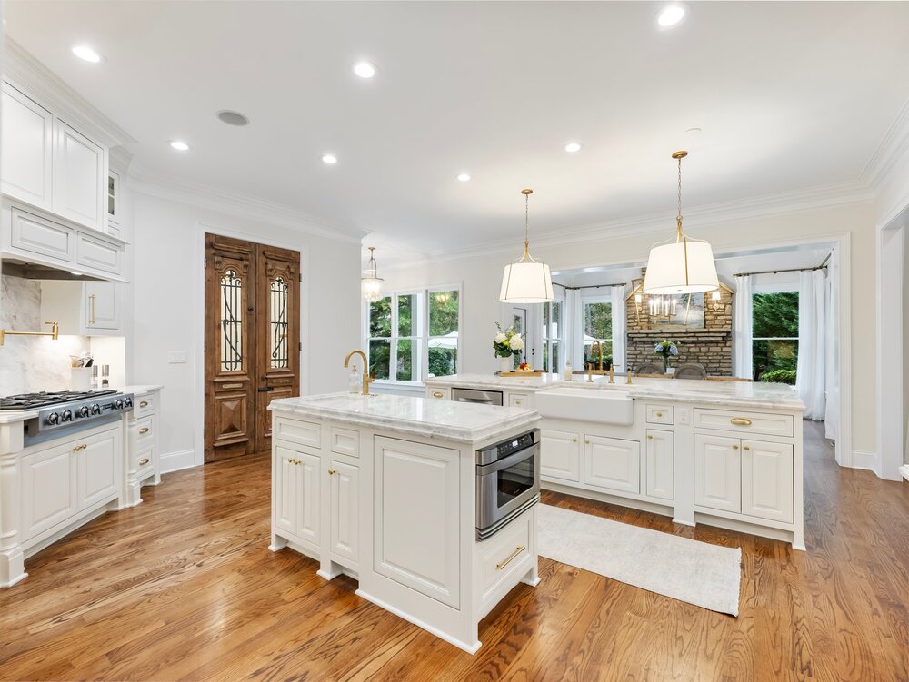 Spacious kitchen with white marble-top counters, stainless steel refrigerator, and stainless steel stovetop over white cabinetry