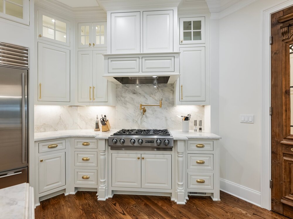 Spacious open-plan kitchen with large white marble-top breakfast island and hanging ceiling lamps, a smaller work island with faucet, and wood double doors