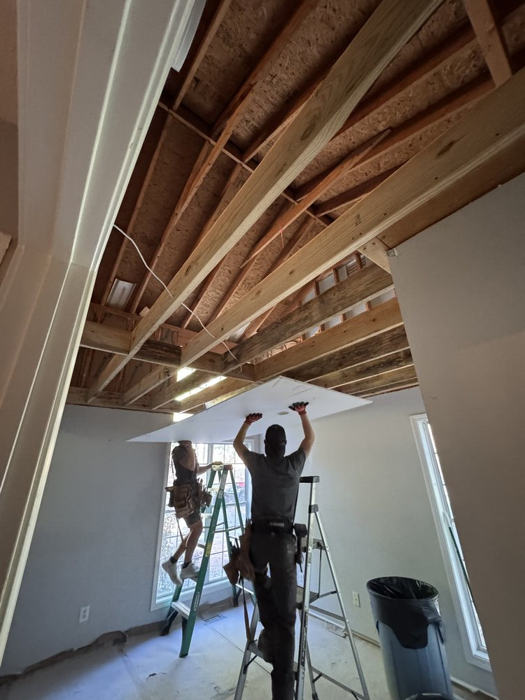 attic space demo in progress and insulation is removed revealing floor joists, and sheet rock being installed onto lower floor ceiling
