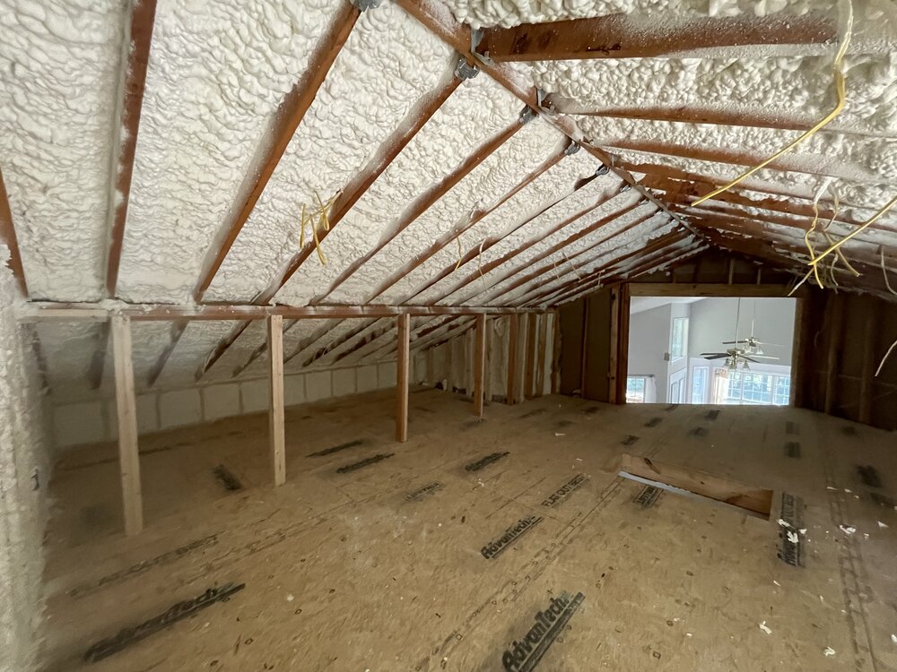 remodel progresses with newly-sprayed insulation on attic ceiling between ceiling joists, new electrical wiring hanging down for light connections
