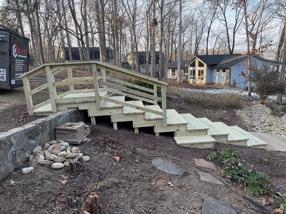 after image of the new staircase with dual ralings leading over the retaining wall and going down to the wood bridge before the house's back deck