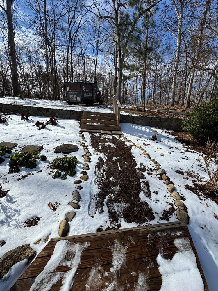 view of the dirt path leading up to the old wooden stairs going over a retaining wall to the upper parking area, and the Kore Handyman shop trailer is in view