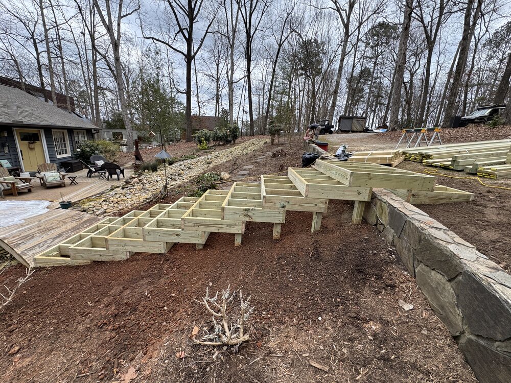 the old stairs have been removed, the dirt area cleaned and new dirt laid down, and a 10-tread staircase has been framed that leads up the slope from the bridge going over the retaining and stepping down into the upper parking area