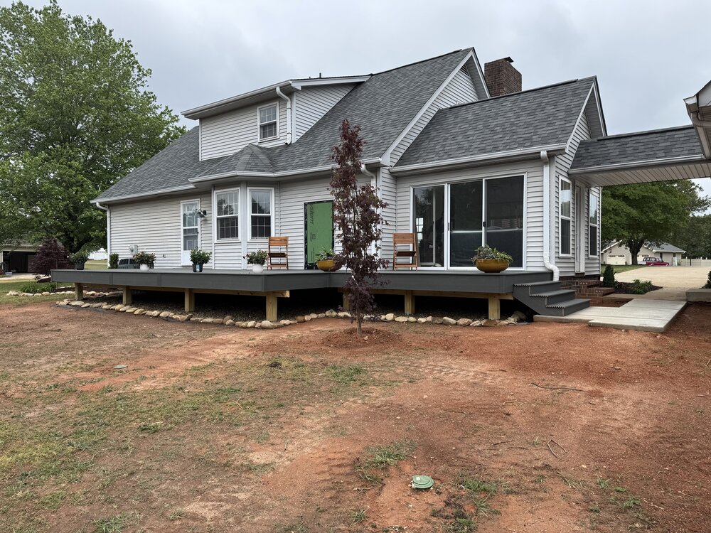 The completed view of the deck and house with plants and furniture on it.