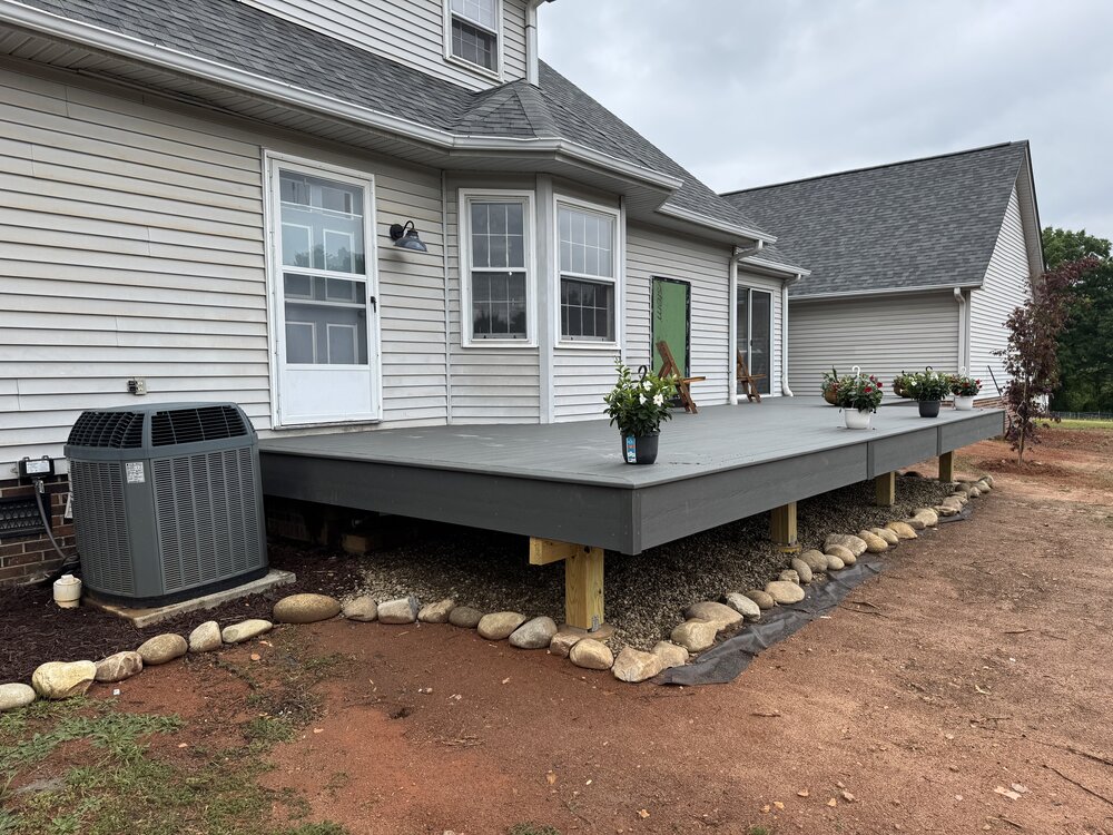 The completed view of the deck and house with plants and furniture on it.