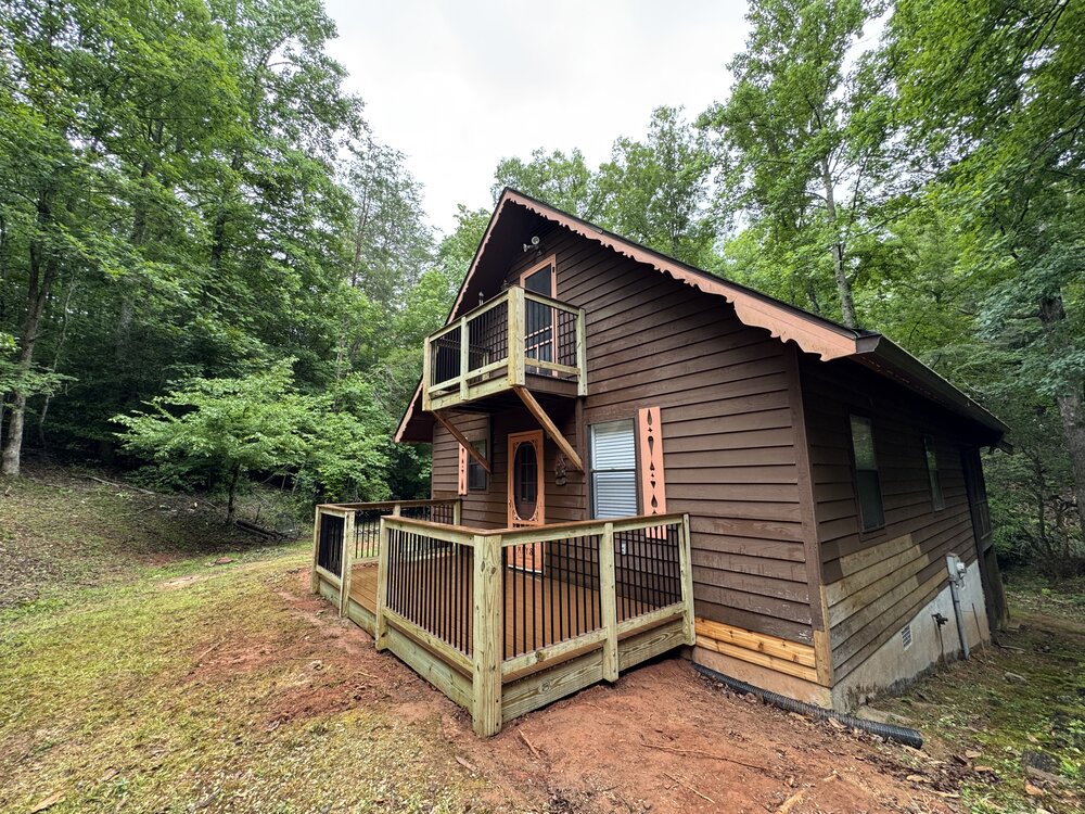 After-photo of the same cabin, seen from a side-view, with a new Trex deck with aluminum picket railings and elegant design.
