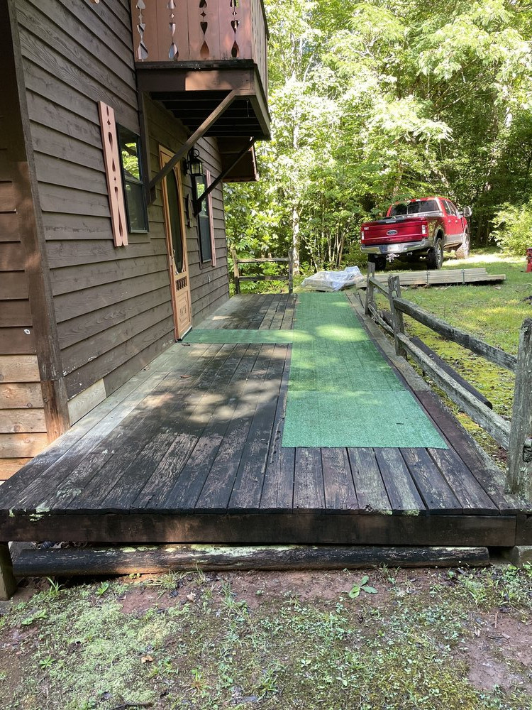 Before-photo of a side-view of a wooden cabin, with a run-down deck, showing dark, rotten boards